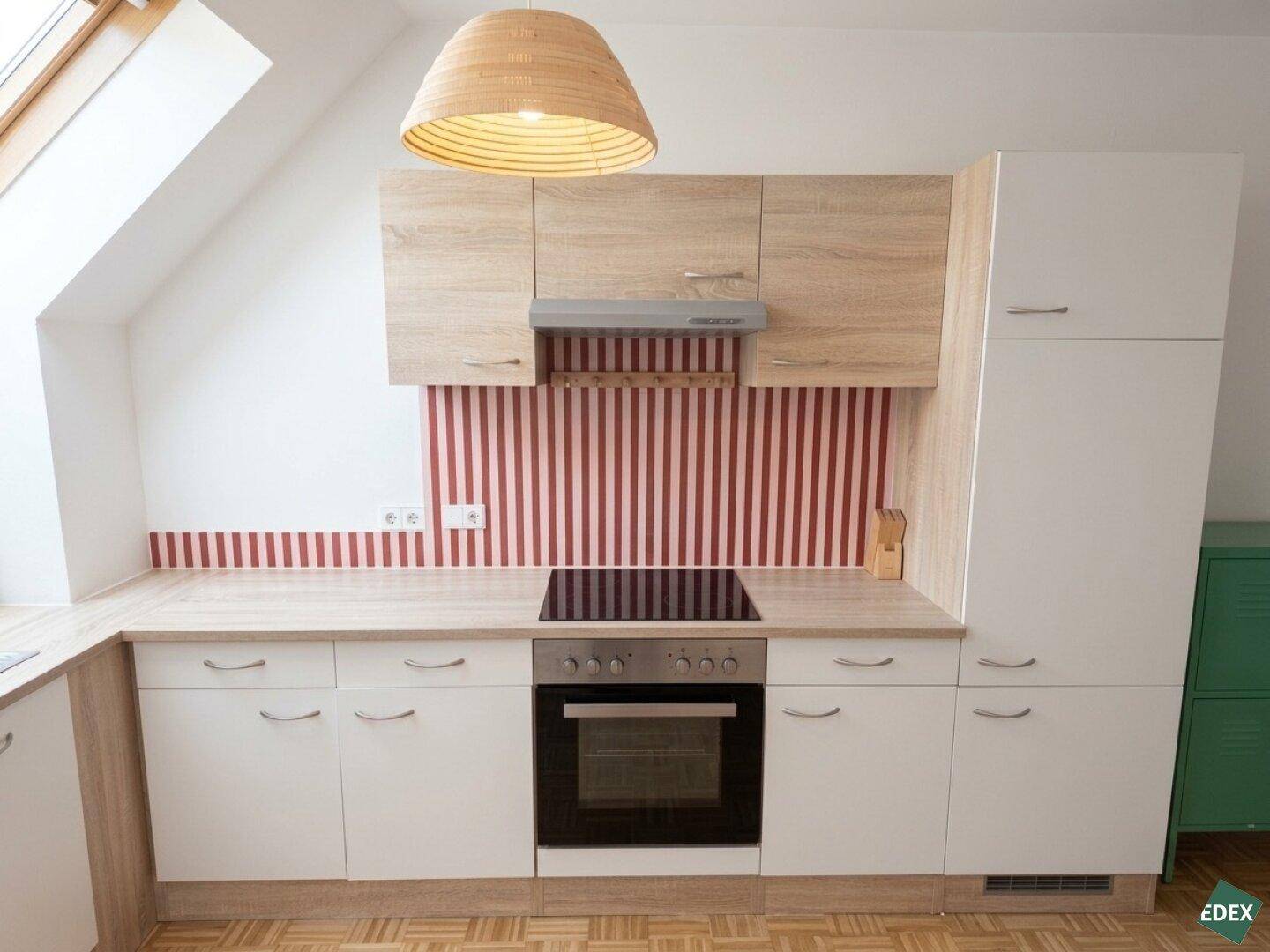 Detailansicht der Küche mit Induktionskochfeld, Backofen, Dunstabzugshaube und gestreifter Rückwand.