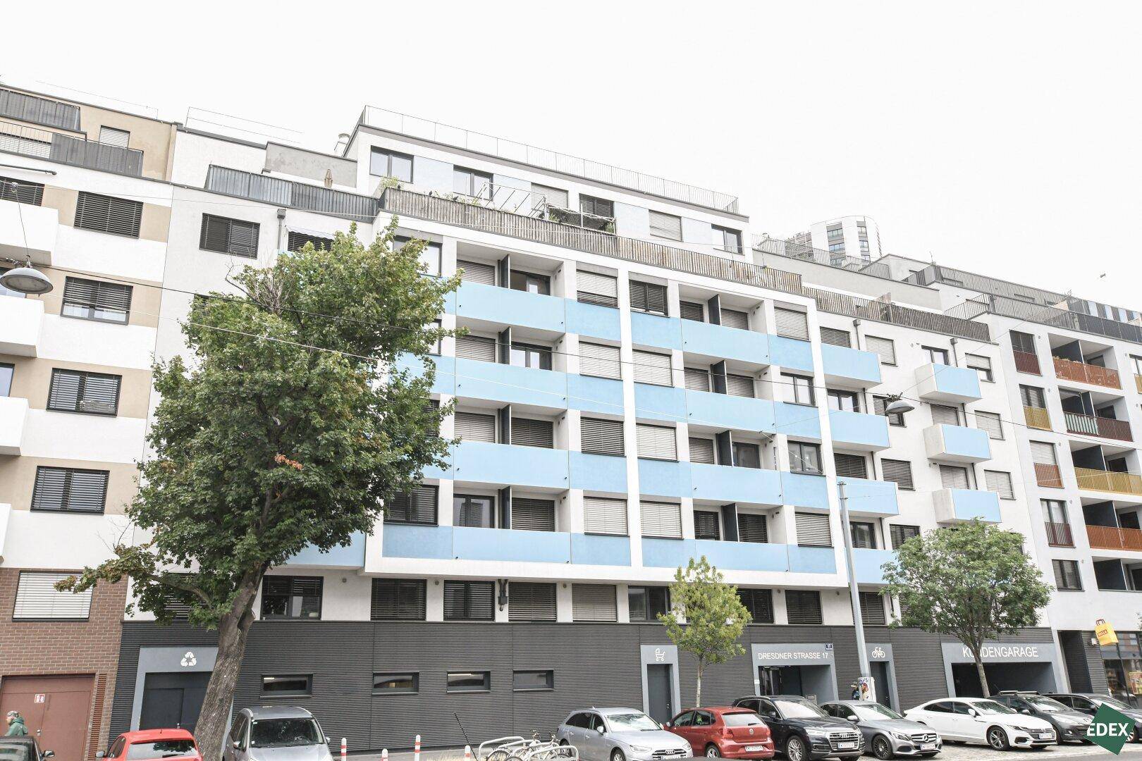 Moderne Wohnhausfassade mit blauen Balkonen und großen Fenstern in urbaner Umgebung.