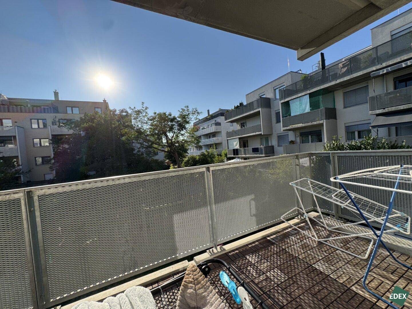 Sonniger Balkon mit Blick auf umliegende Wohngebäude und viel Grün, ideal zum Entspannen.