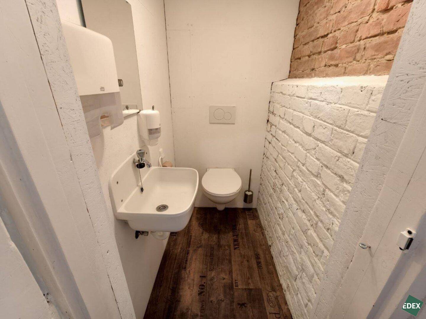 Kleine Gästetoilette mit Waschbecken, WC und einer weiß gestrichenen Ziegelwand.