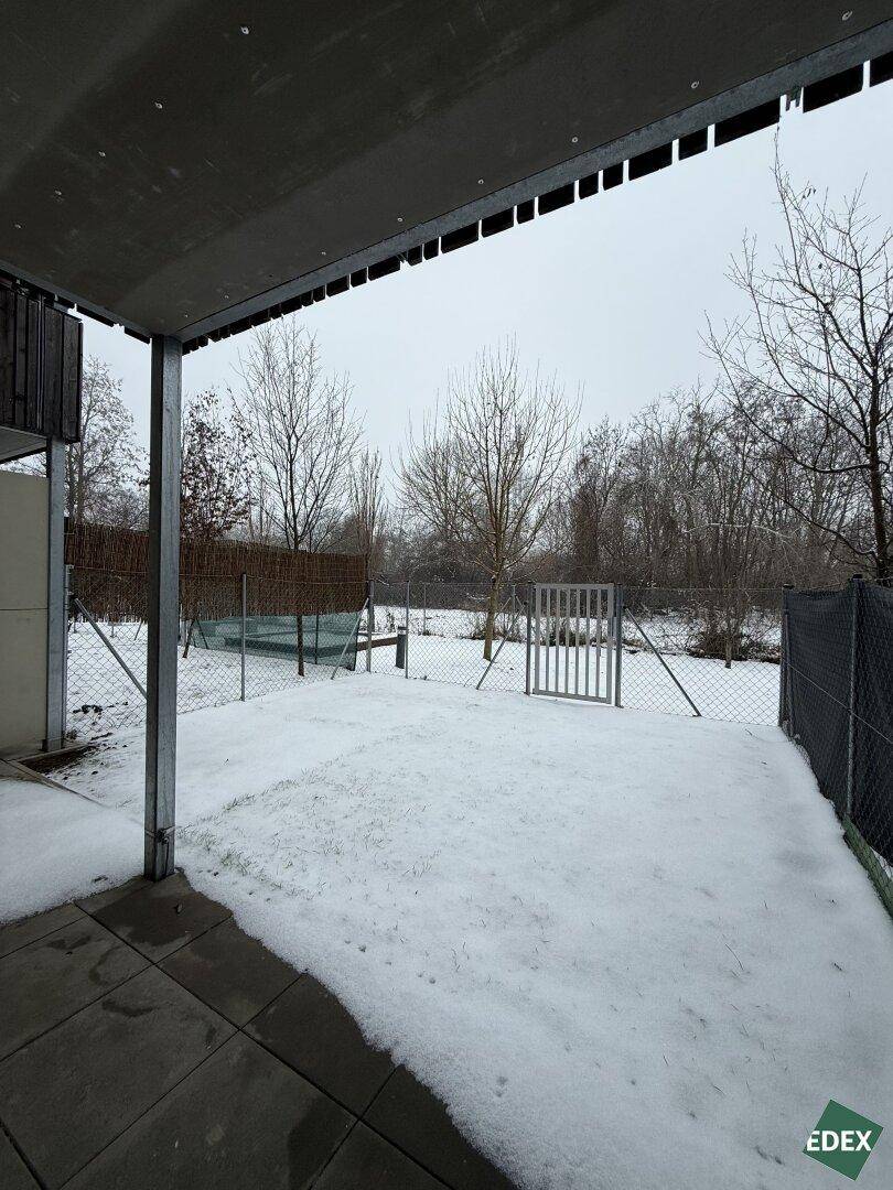 Schneebedeckter Gartenbereich mit überdachter Terrasse und Blick ins Grüne im Winter.
