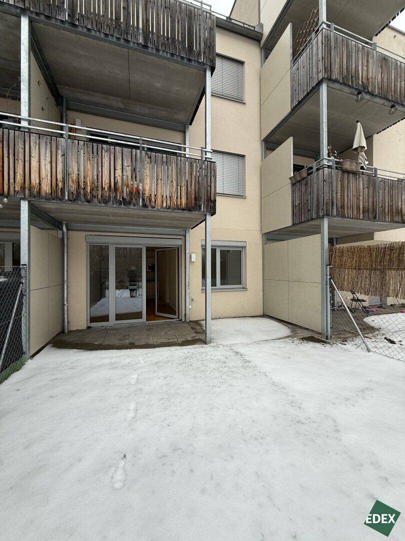 Mehrfamilienhausfassade mit mehreren Balkonen und schneebedecktem Gartenbereich im Erdgeschoss.