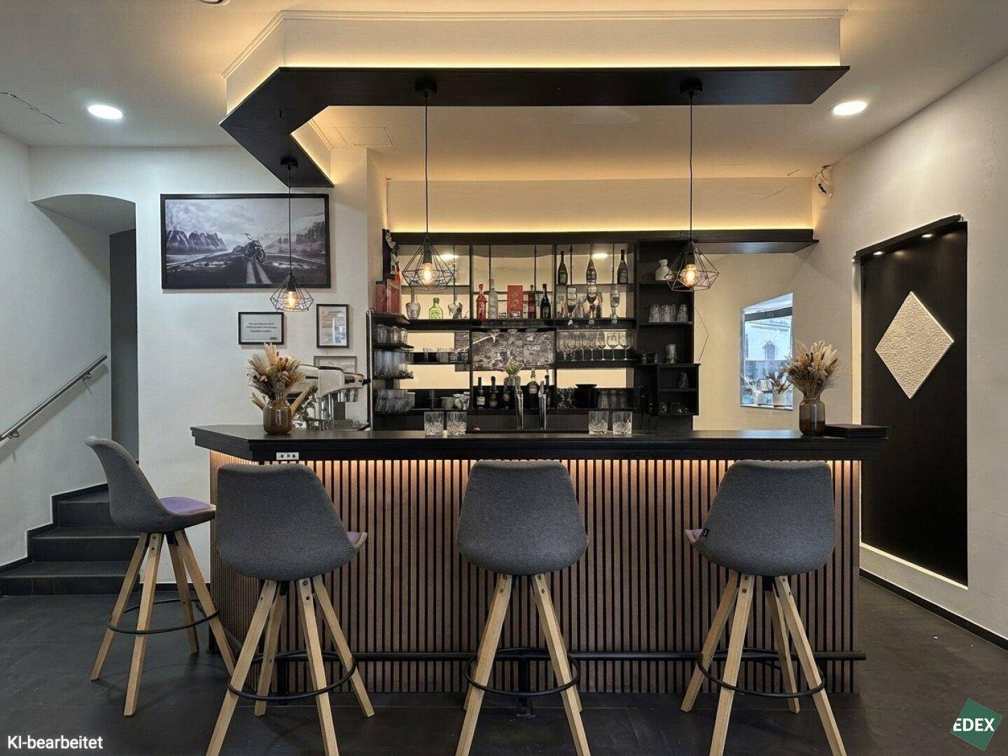 Stilvolle Bar mit dunkler Holztheke, passenden Barhockern und indirekter Beleuchtung, ergänzt durch eine Treppe.