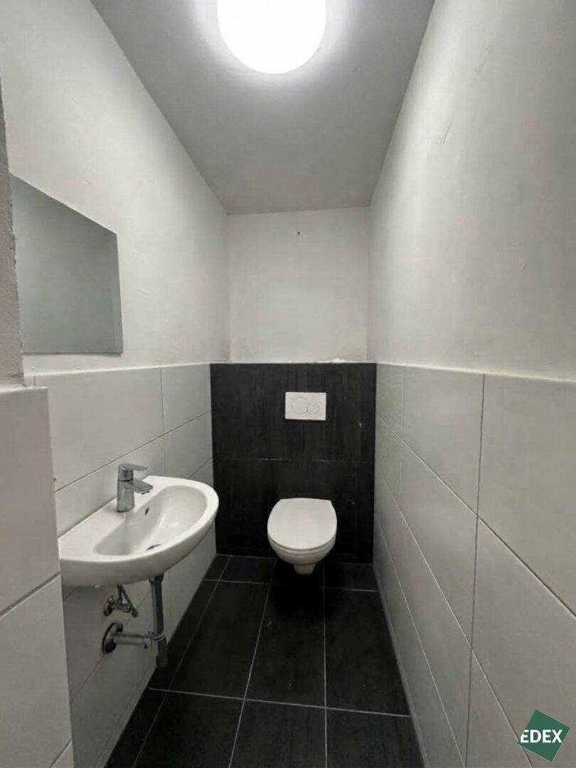 Saubere Gästetoilette mit modernem Wand-WC, Waschbecken und dunklen Bodenfliesen.