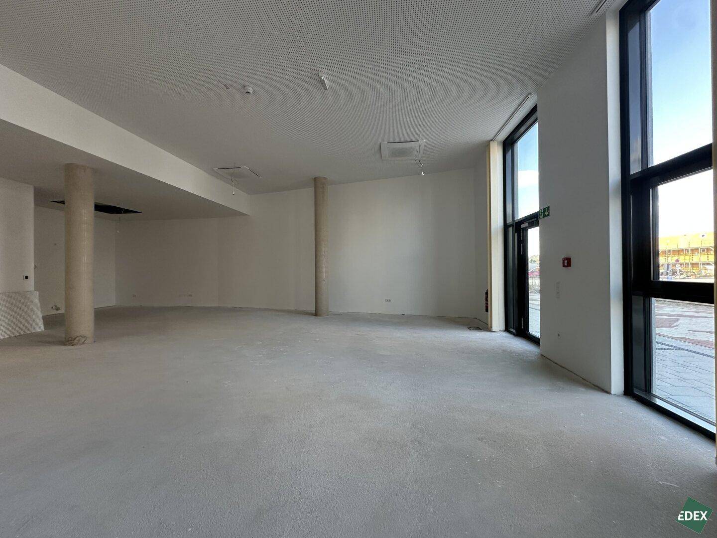 Weiterer Blick in den großen, leeren Gewerberaum mit Betonboden und raumhohen Fenstern, bereit für den Ausbau.
