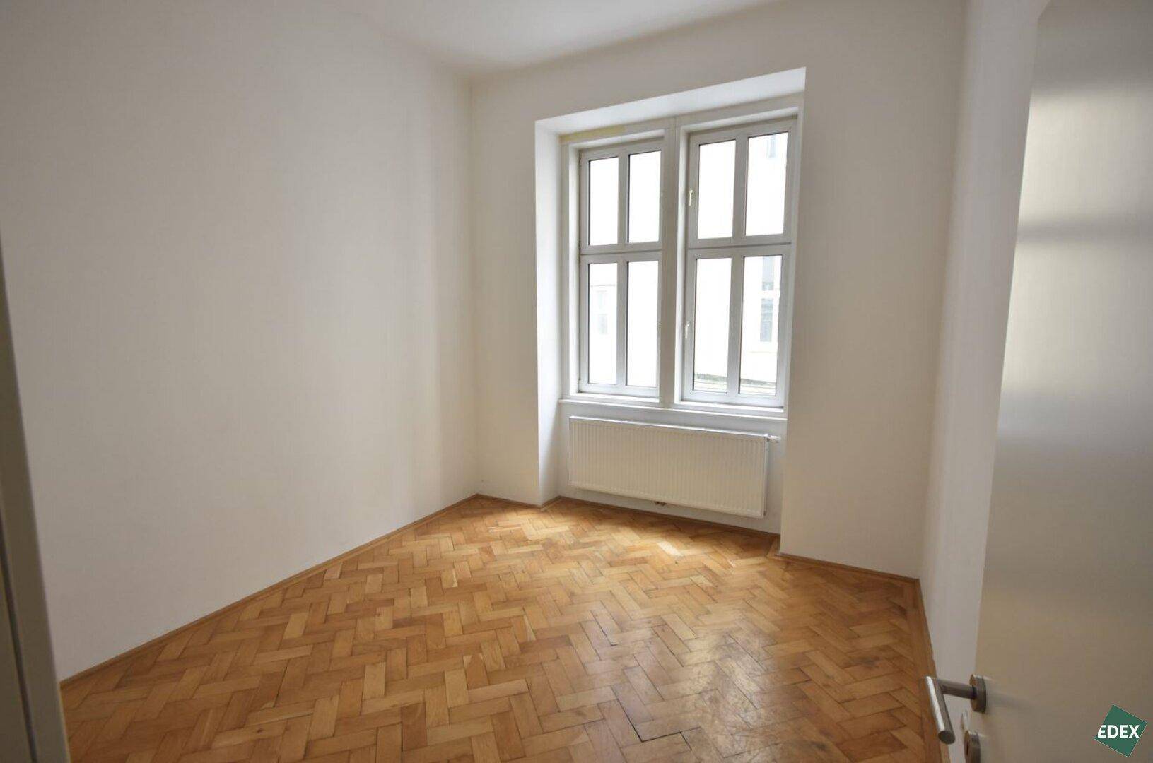 Helles und leeres Zimmer mit schönem Fischgrätparkett und einem großen Fenster für viel Licht.