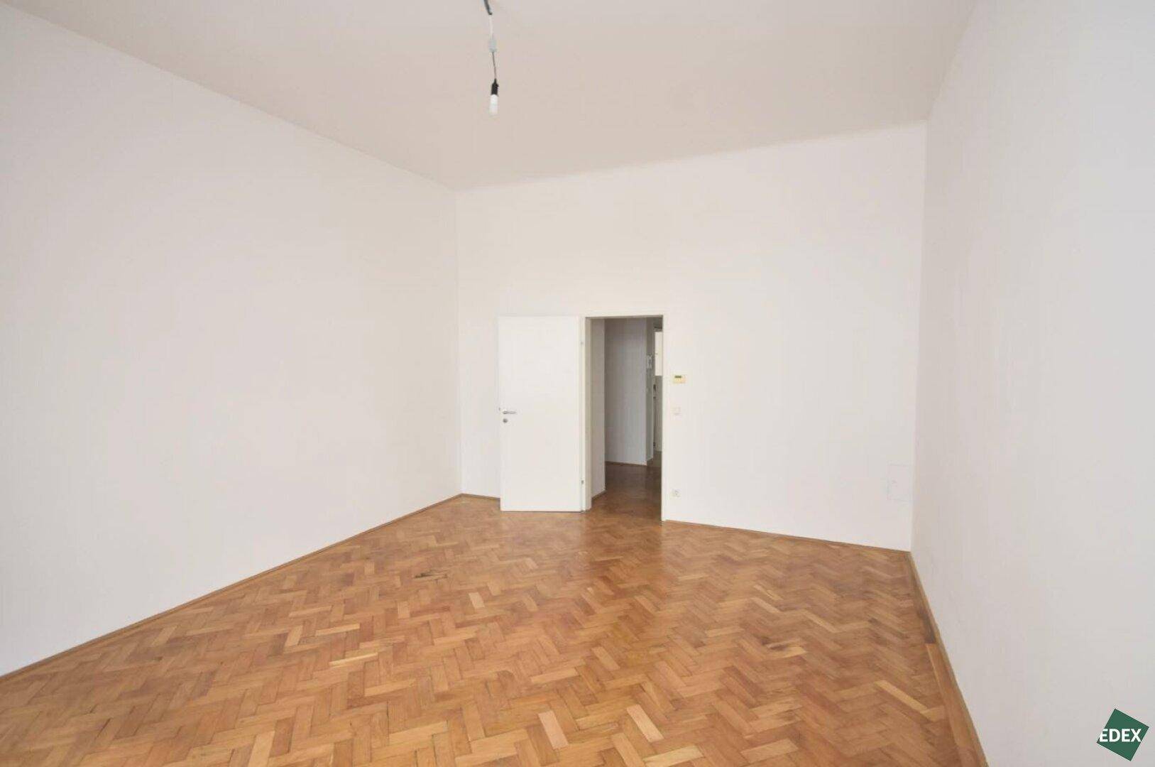 Leeres Zimmer mit elegantem Fischgrätparkett und weiß gestrichenen Wänden, bereit zur individuellen Gestaltung.