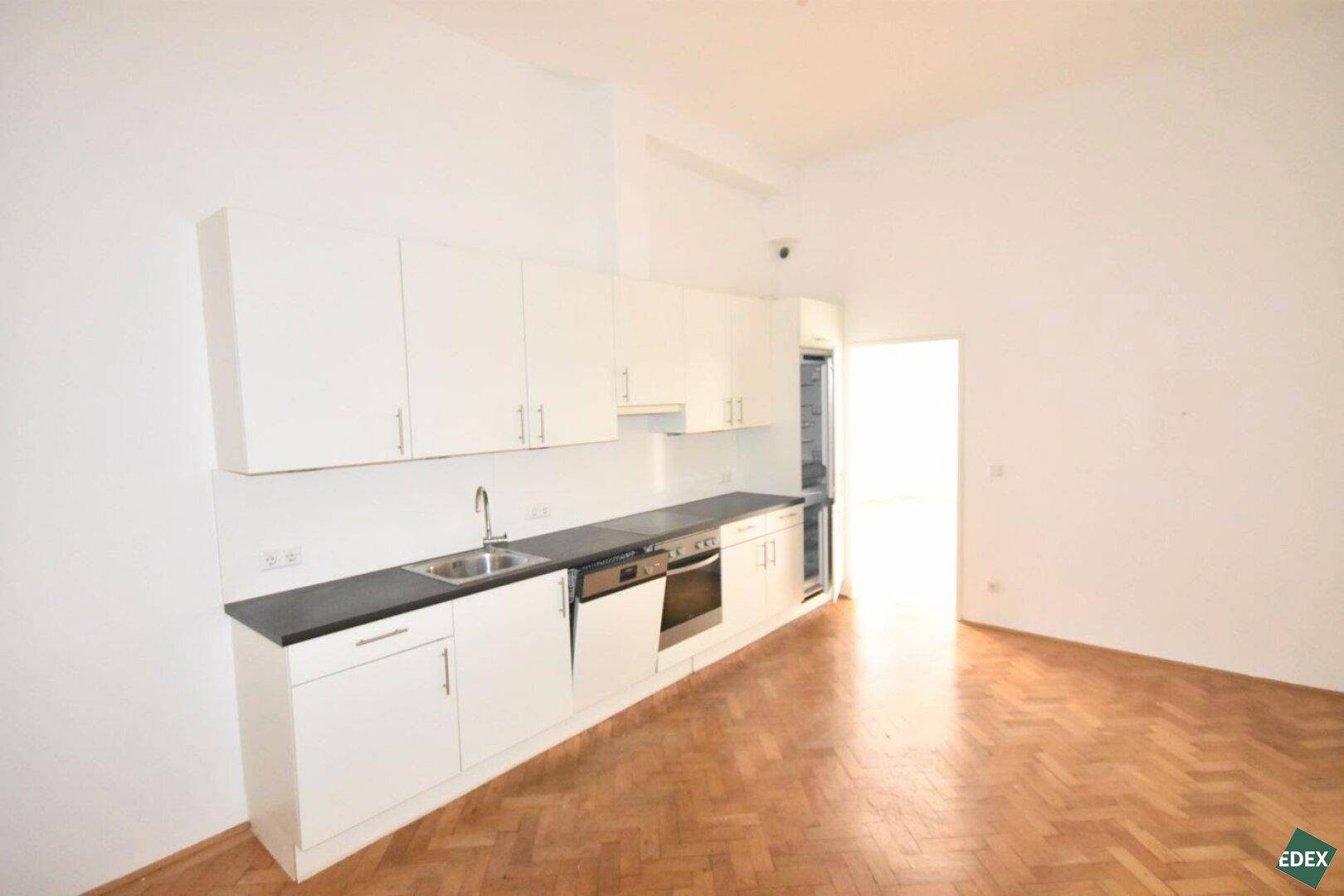 Moderne Einbauküche mit weißen Fronten, dunkler Arbeitsplatte und Kühlschrank, ideal für offenes Wohnen.