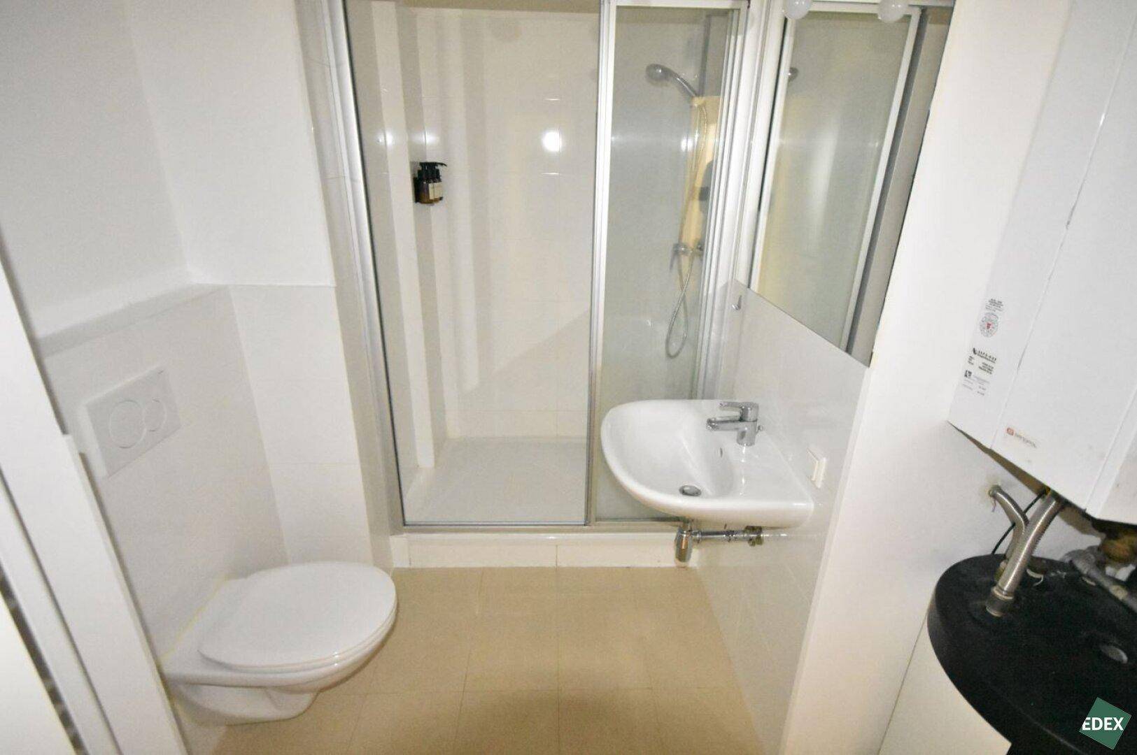 Kompaktes Badezimmer mit Duschkabine, WC und Waschbecken, hell gefliest und funktional.