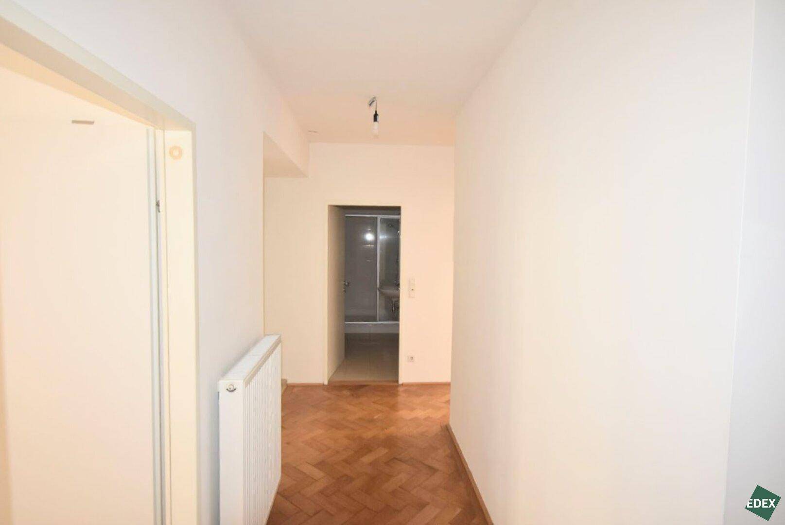 Heller Flur mit Fischgrätparkett und Zugang zu einem Badezimmer mit Duschkabine.