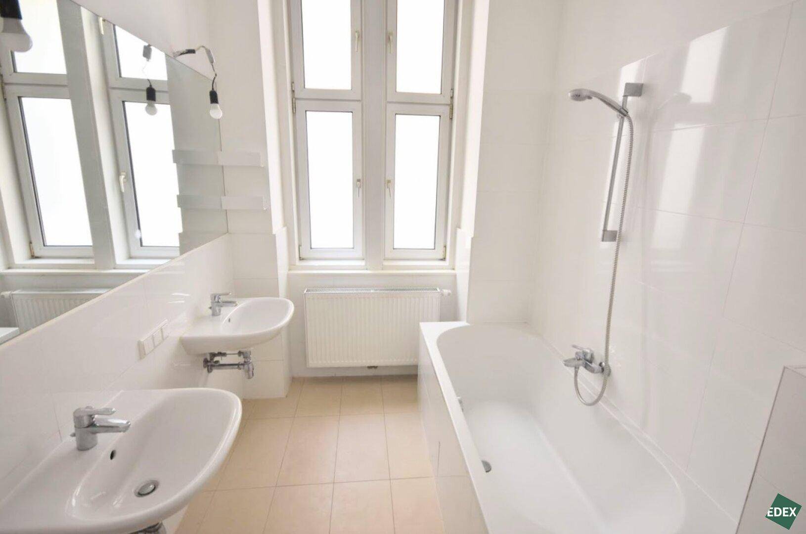 Geräumiges Badezimmer mit Badewanne, zwei Waschbecken und großem Fenster für natürliches Licht.