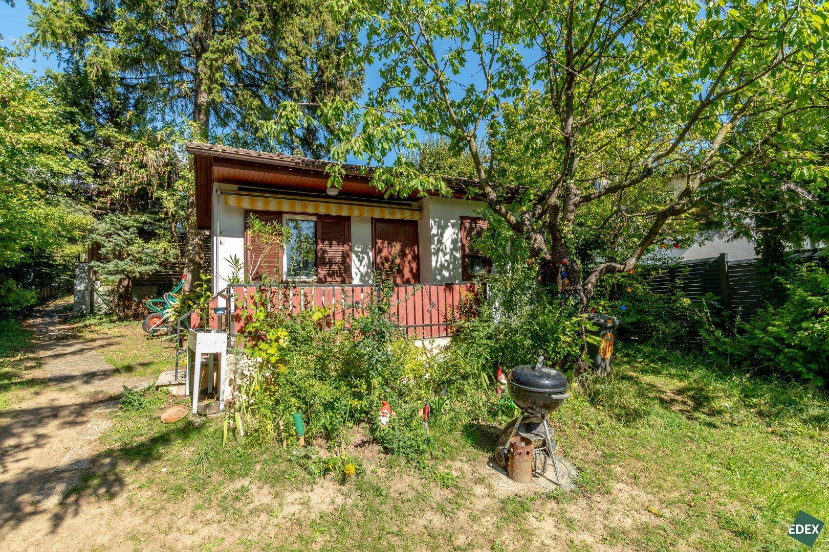 Vorderansicht des Gartenhauses mit kleiner Veranda, umgeben von einem grünen Garten mit Grill.