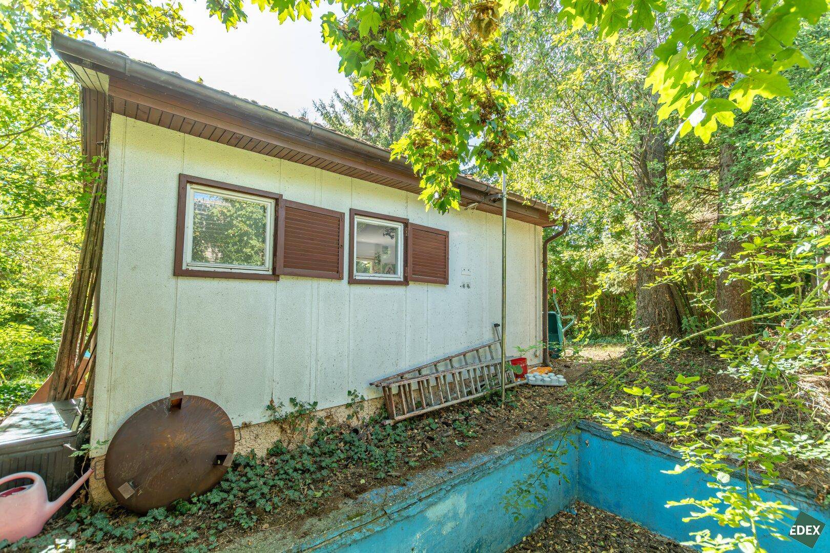 Seitenansicht des Gartenhauses mit Fensterläden und einem ungenutzten Poolbereich im Vordergrund.