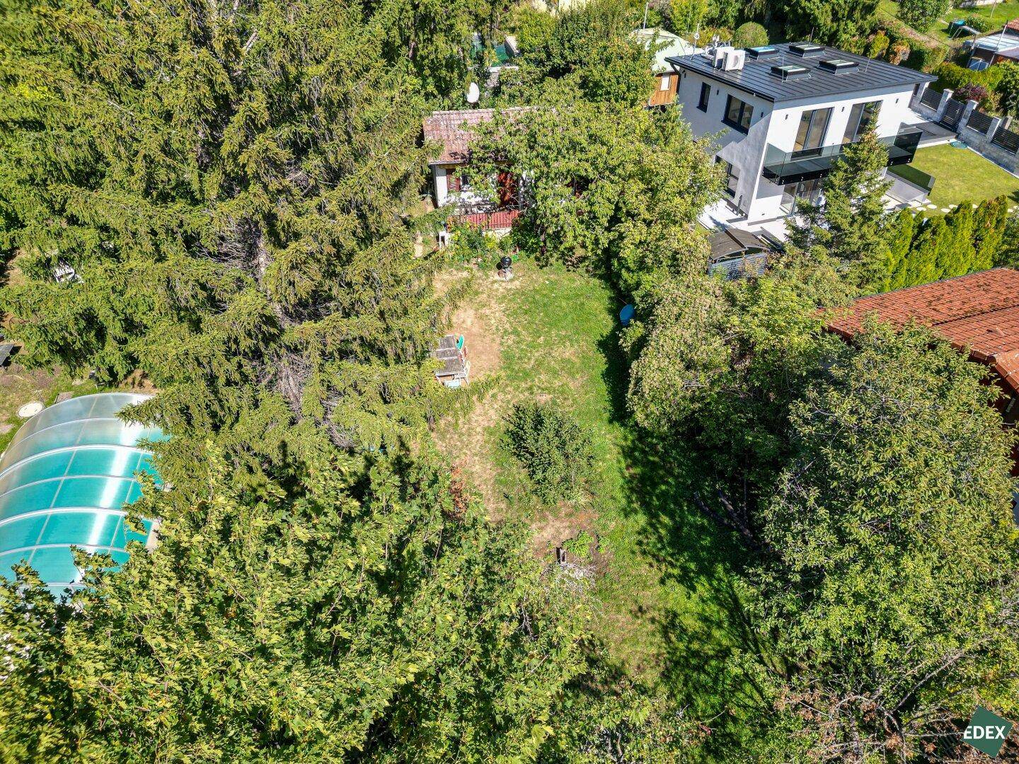 Luftaufnahme des Grundstücks mit Gartenhaus, umgeben von Bäumen und benachbarten Häusern.