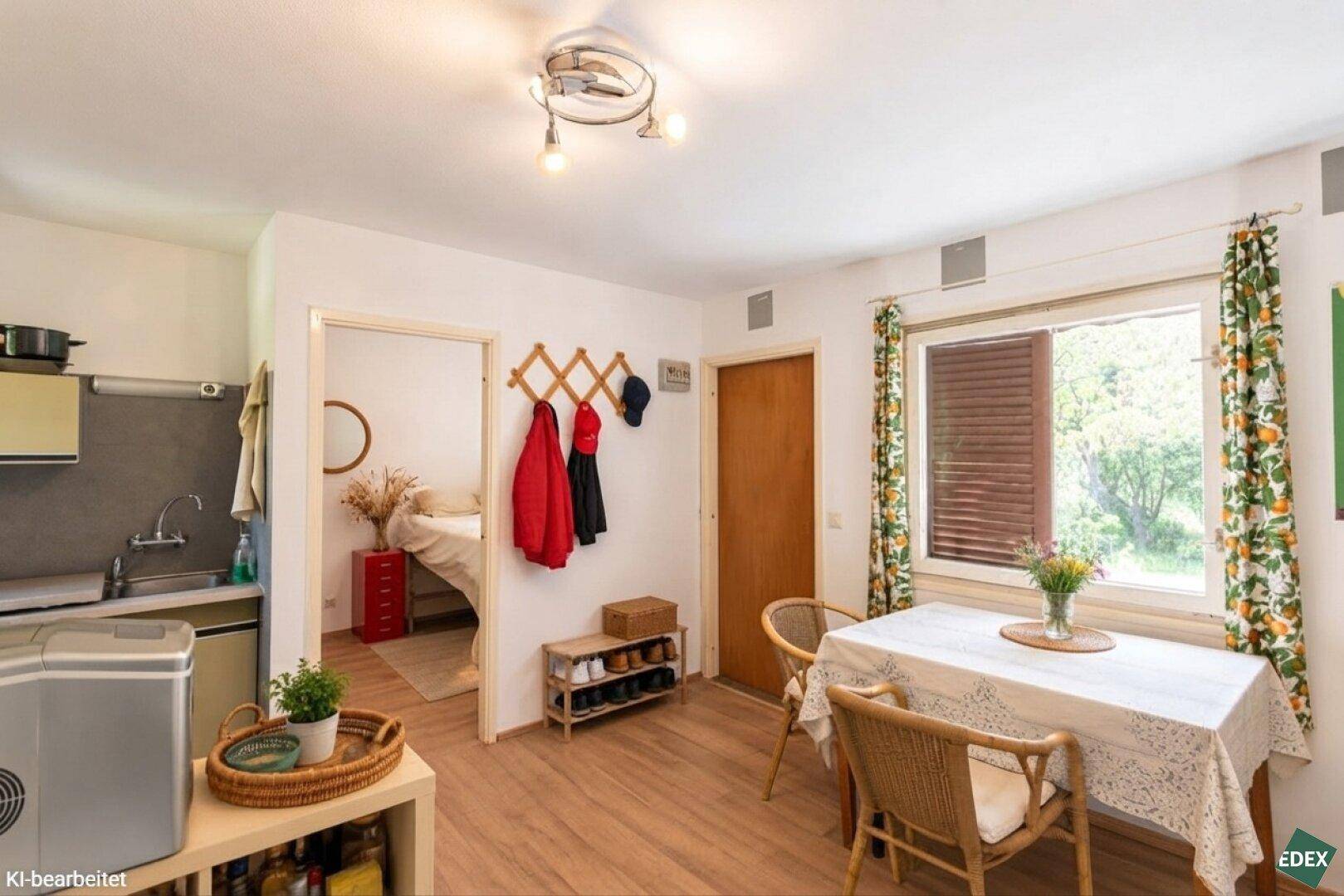 Heller Wohn-Essbereich mit Esstisch, Laminatboden und Zugang zu Schlafzimmer und Kochnische.