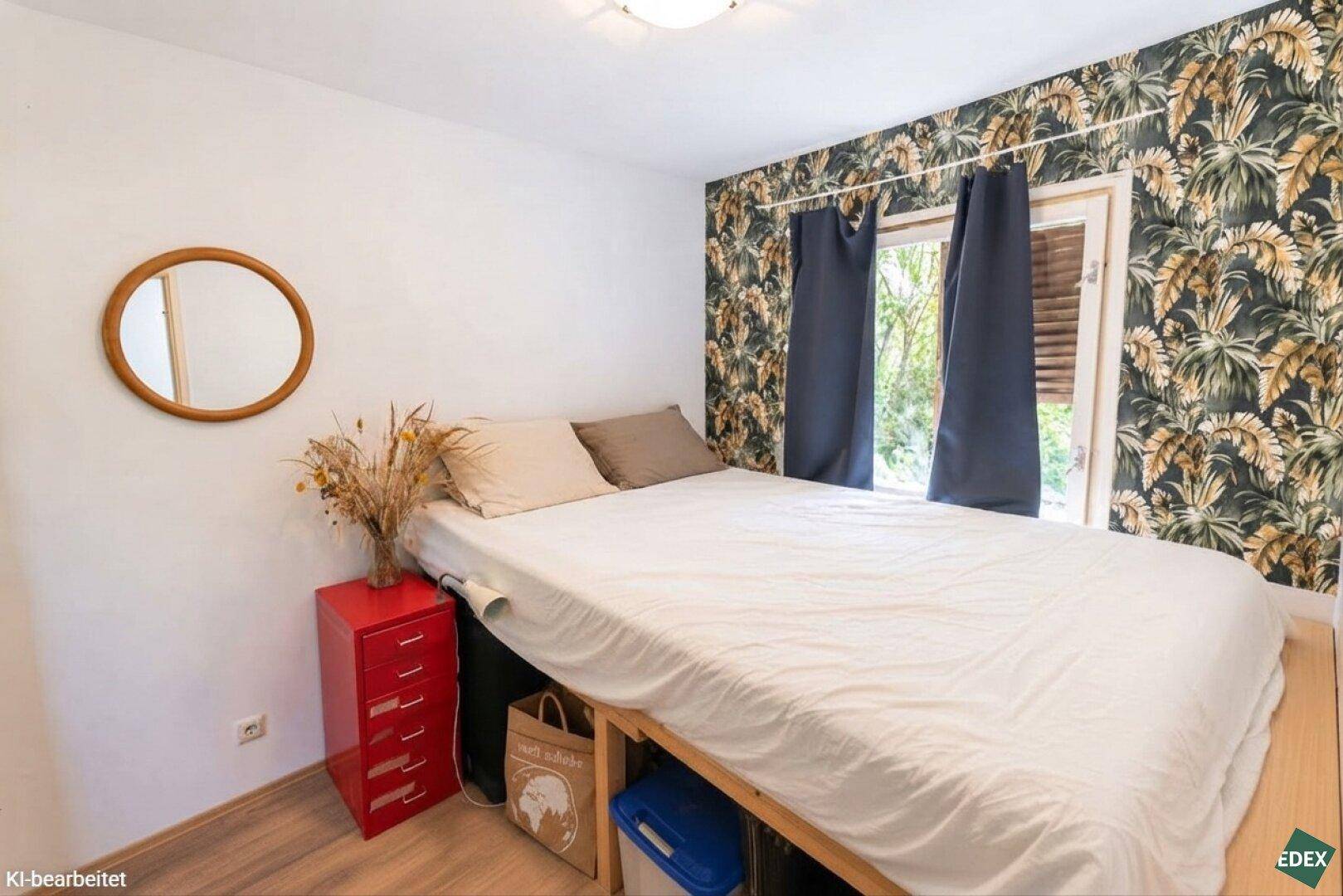 Schlafzimmer mit Bett, Nachttisch und Fenster, akzentuiert durch eine Tapete mit Pflanzenmuster.