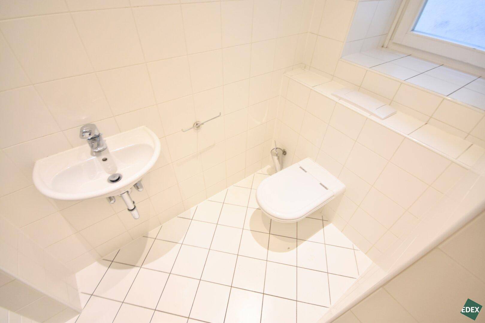 Separates WC mit Toilette, kleinem Waschbecken und Fenster für natürliche Belüftung.