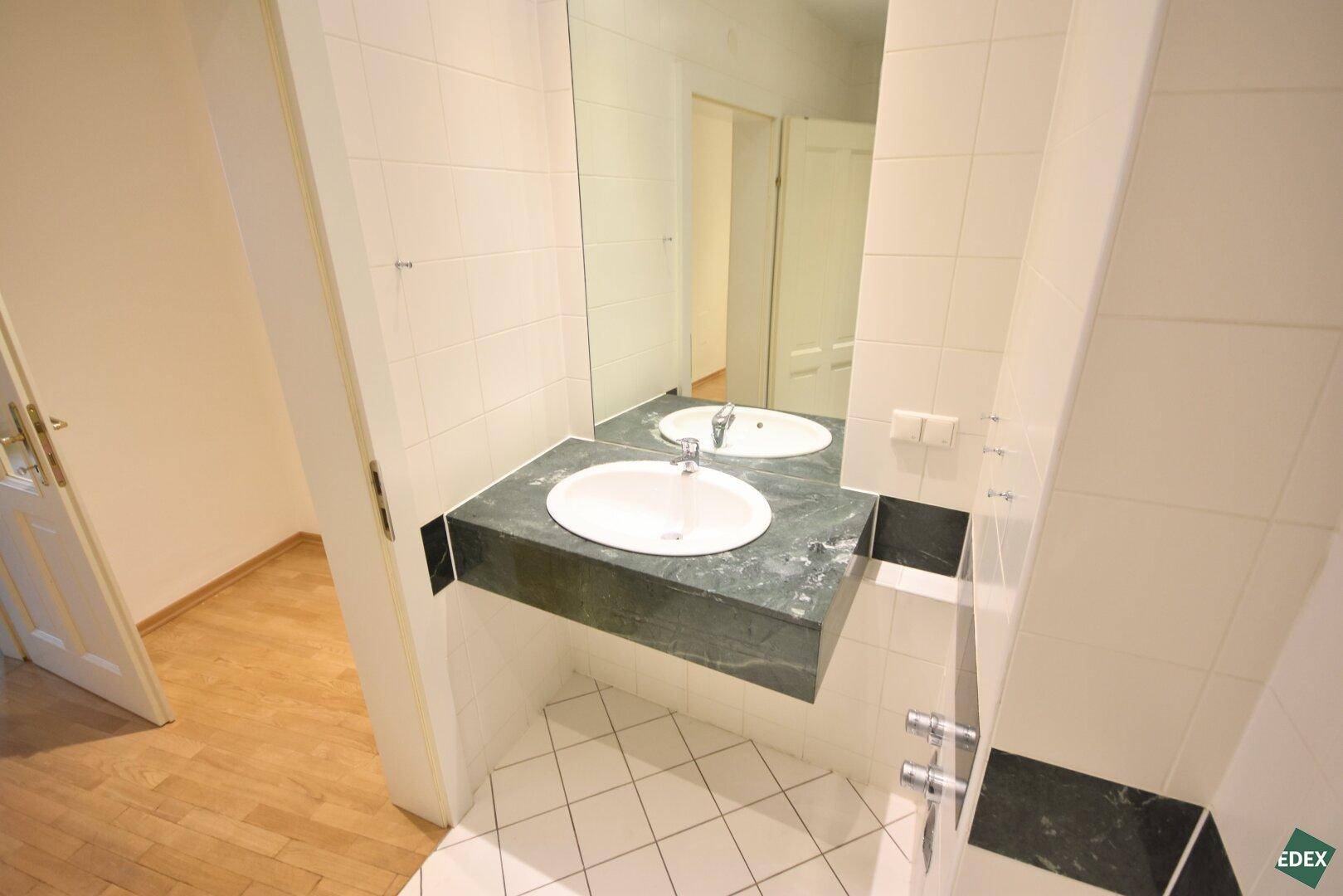Badezimmer mit Einzelwaschbecken, großem Spiegel und dunkler Marmor-Waschtischplatte.