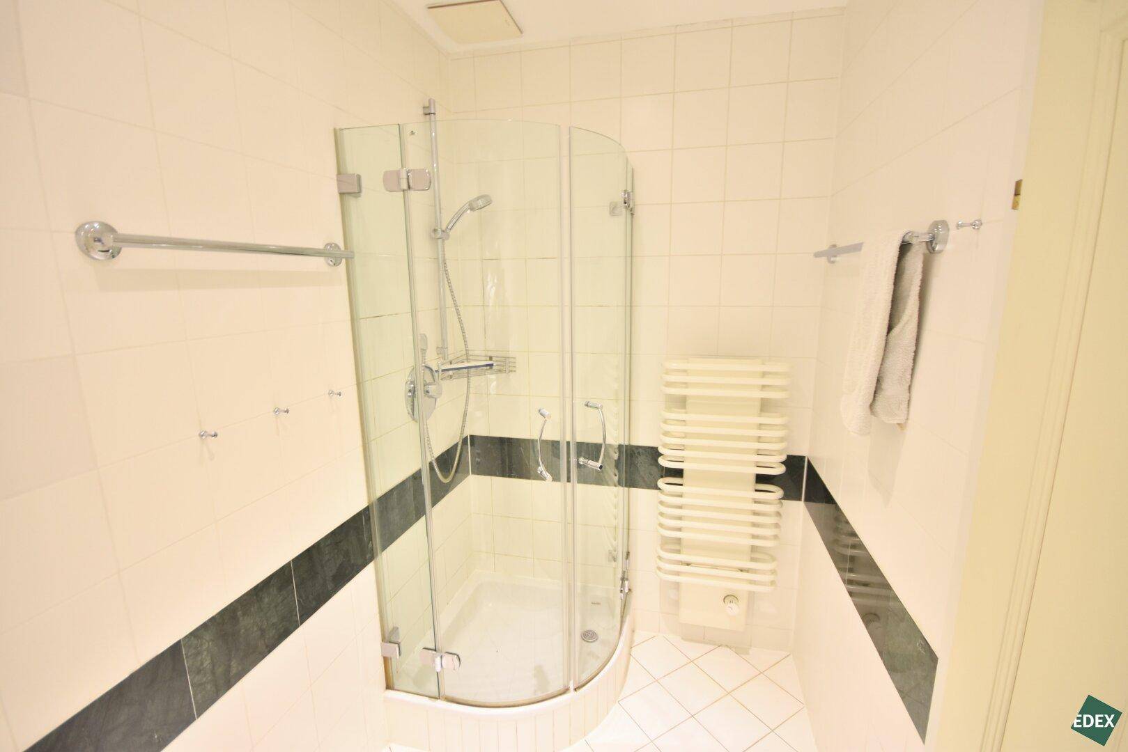 Modernes Badezimmer mit weiß gefliesten Wänden, Eckdusche und beheiztem Handtuchhalter.