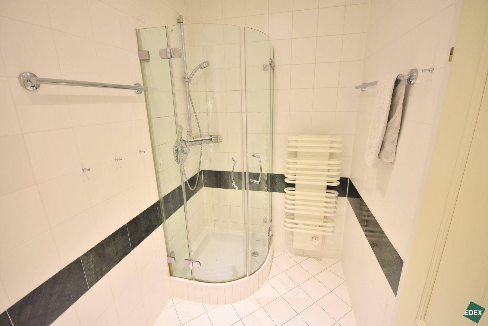 Helles Badezimmer mit Duschkabine, weißen Fliesen und praktischem Handtuchheizkörper.