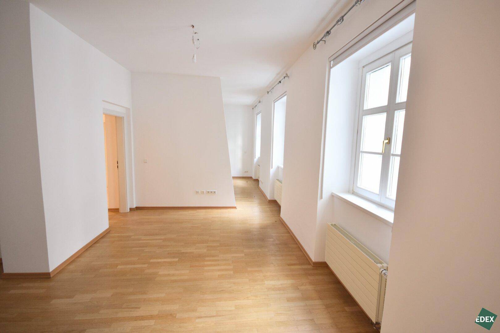 Geräumiges, helles Zimmer mit Holzparkett und mehreren Fenstern für viel Tageslicht.