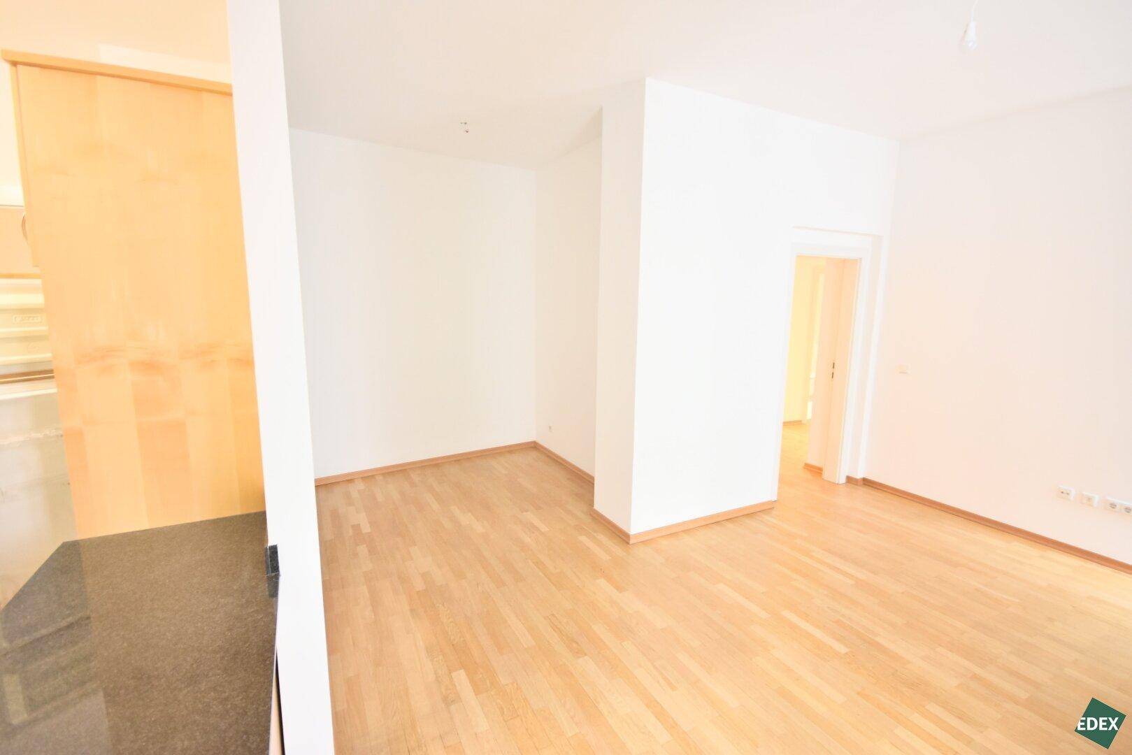 Offener Wohnbereich mit Parkettboden und Zugang zur Küche, ideal für modernes Wohnen.