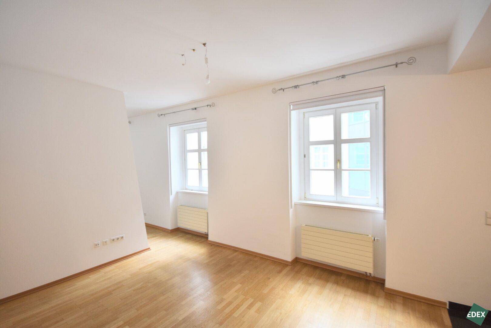 Freundliches Zimmer mit hellem Parkettboden und zwei Fenstern, ideal für Wohn- oder Schlafbereich.