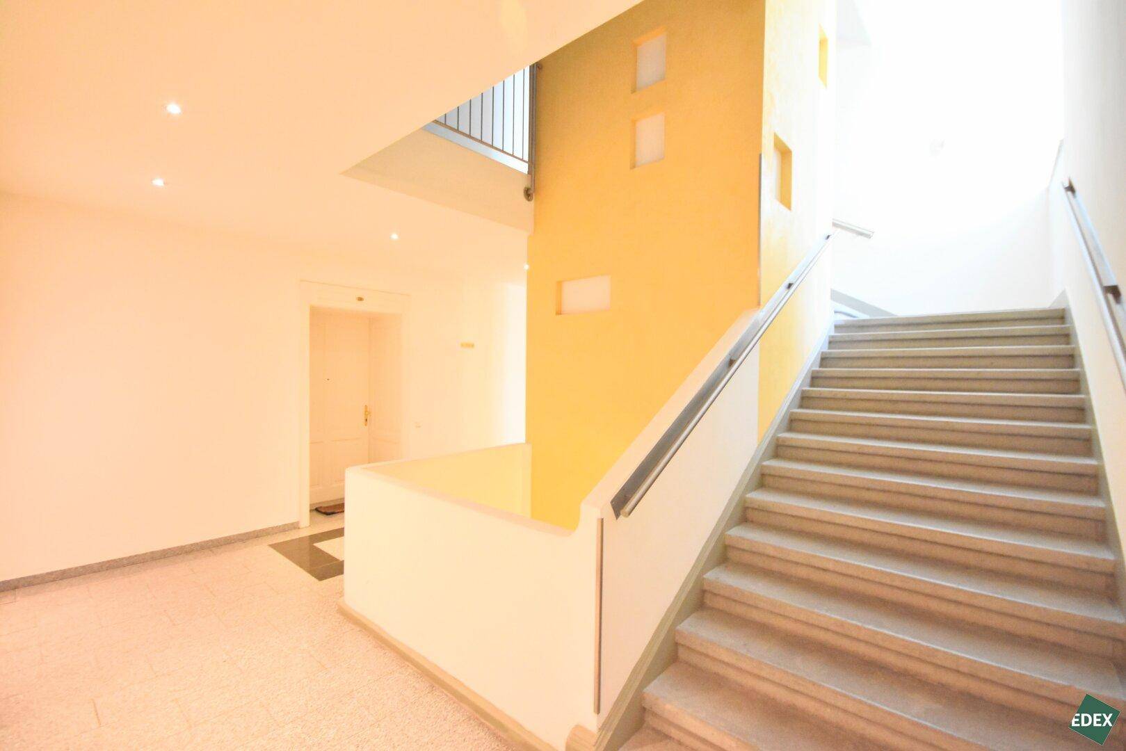 Helles Treppenhaus mit Steinstufen und gelb akzentuierter Wand im Gemeinschaftsbereich.