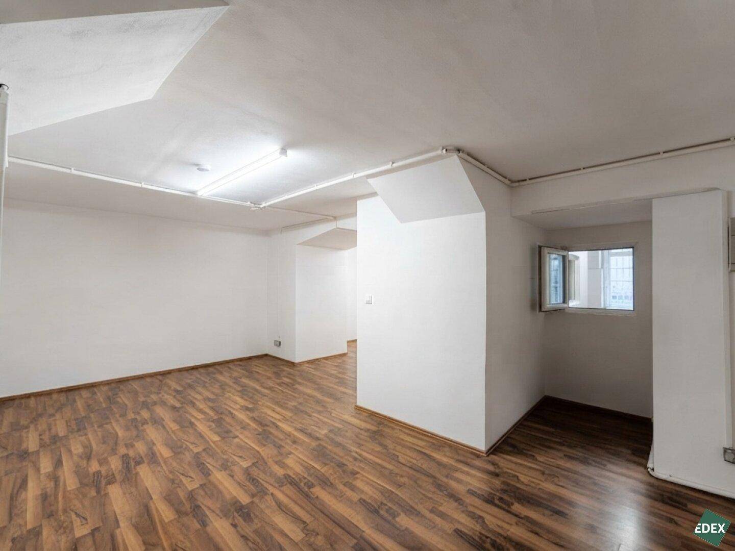 Schlichter Innenraum mit weißen Wänden, Laminatboden und einem kleinen Fenster.