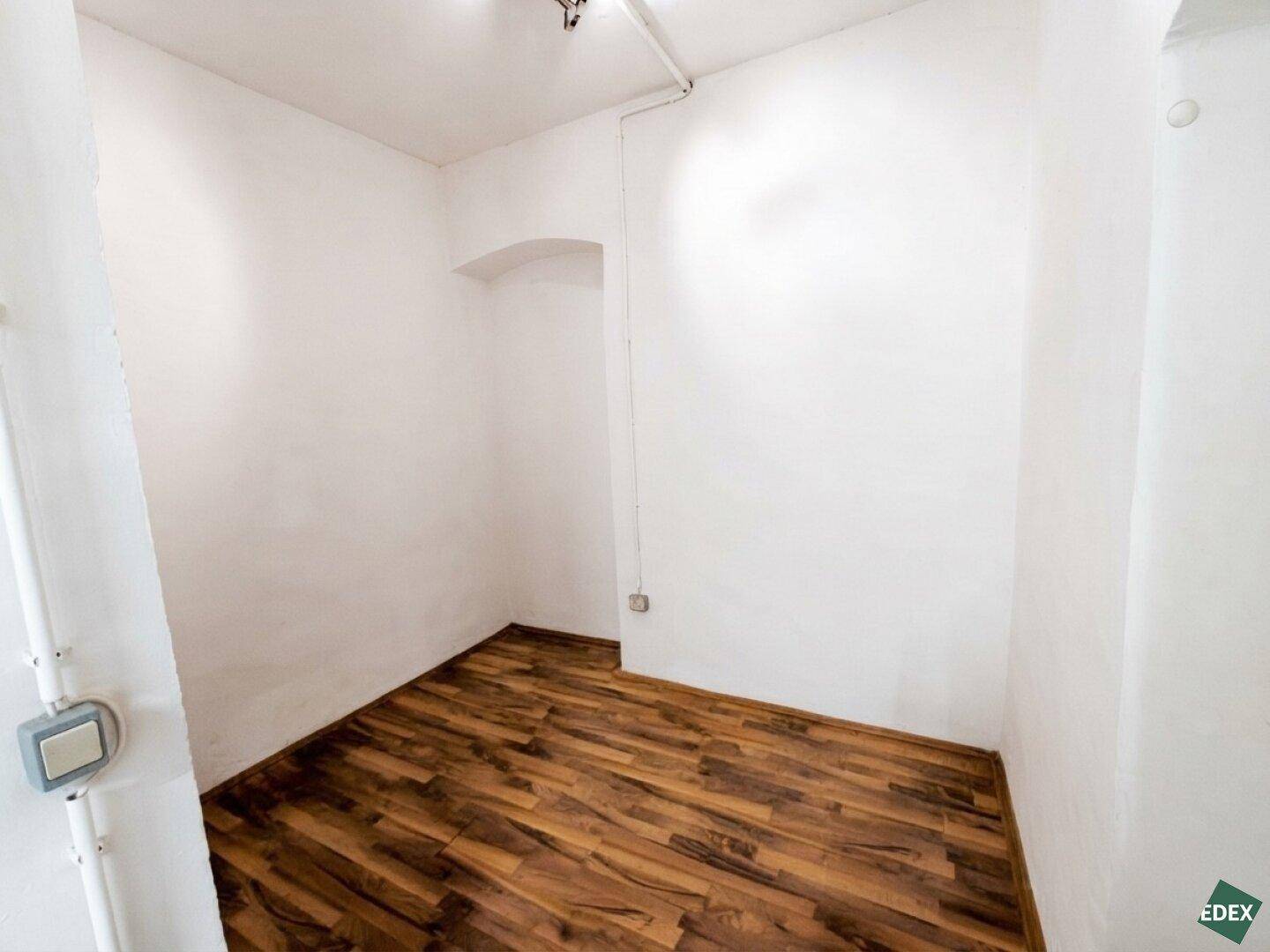 Kleiner, leerer Raum mit weißen Wänden, Laminatboden und einer Nische.