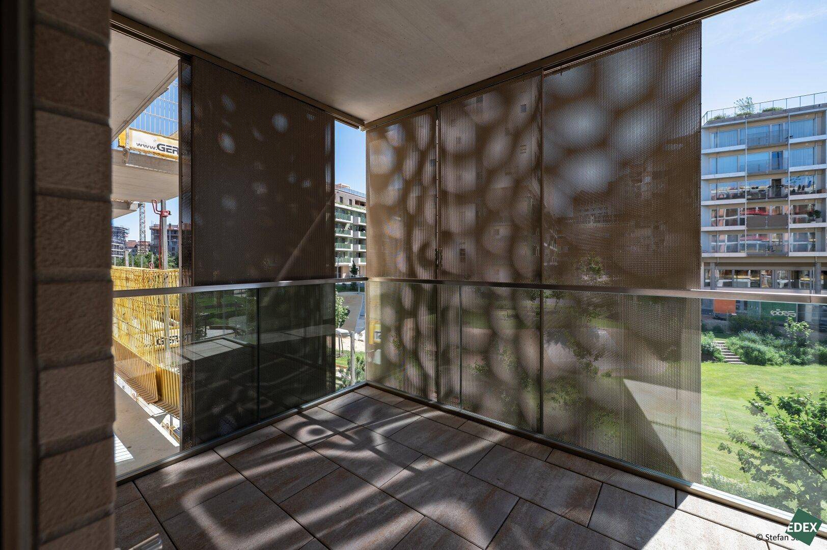 Moderner Balkon mit Fliesenboden und perforierten Sichtschutzelementen, bietet Blick auf Grünflächen.