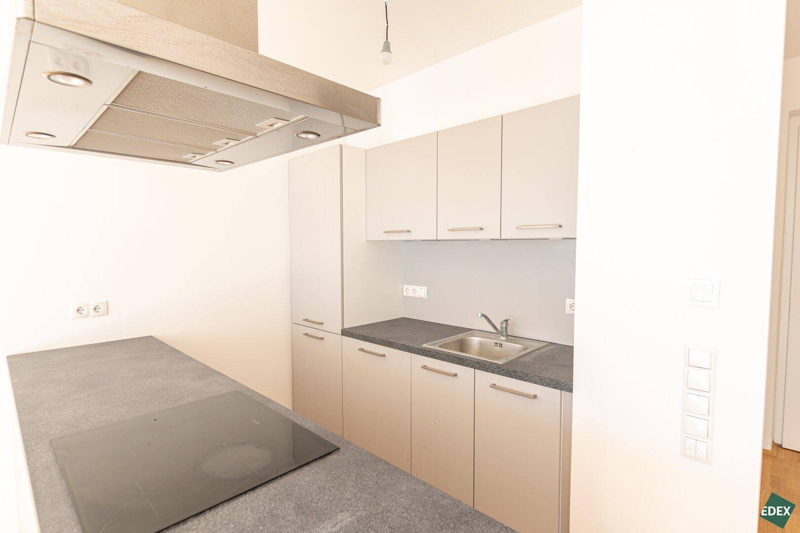 Moderne Einbauküche mit grauen Schränken, Induktionskochfeld und Dunstabzugshaube.