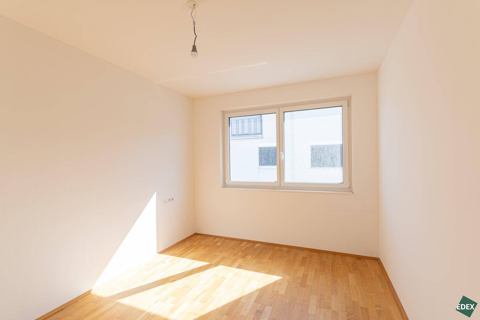 Helles Schlafzimmer mit Holzboden und einem Fenster, das viel Tageslicht hereinlässt.