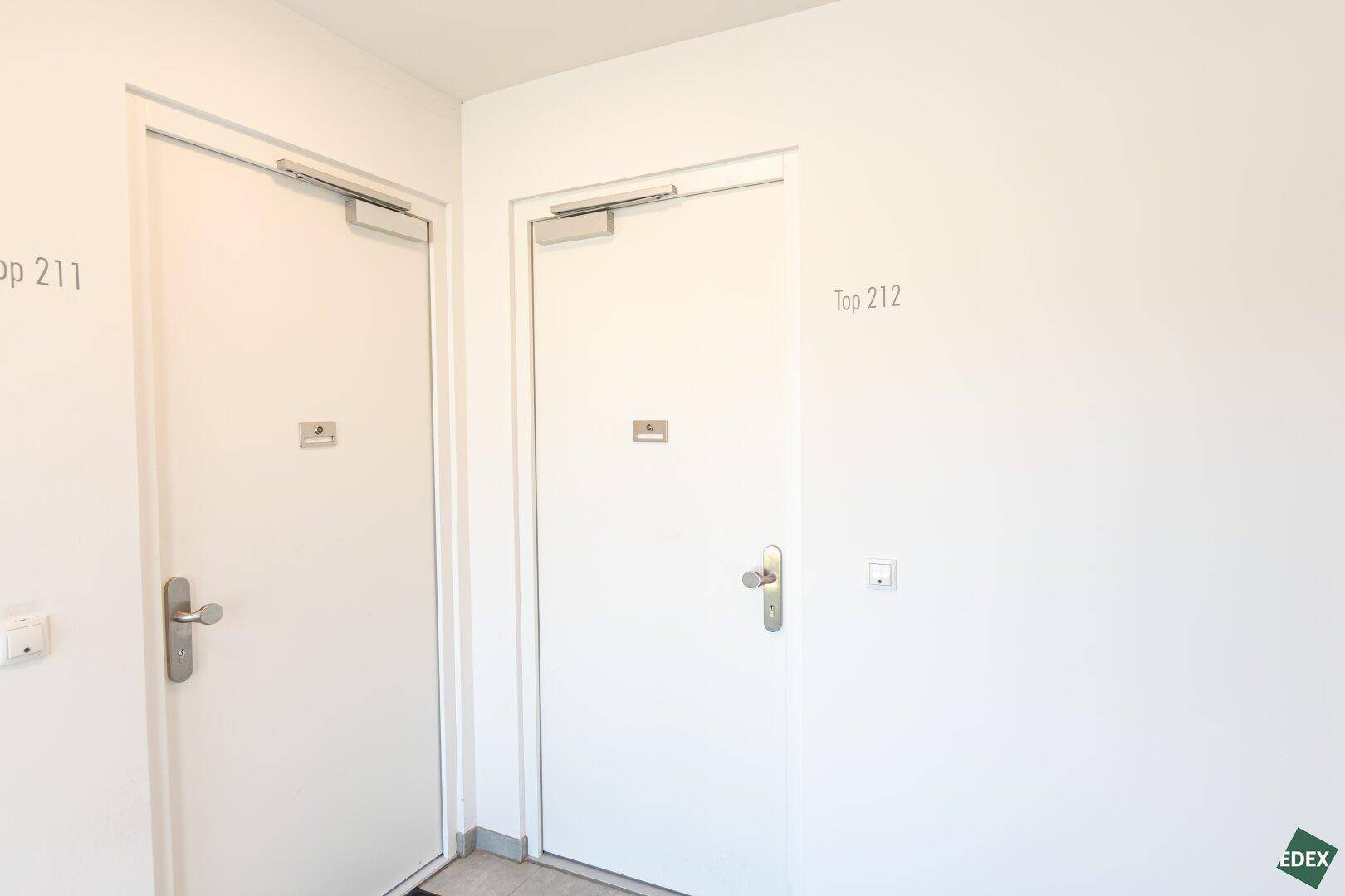 Heller Flur mit zwei Wohnungstüren, die zu den Einheiten Top 211 und Top 212 führen.