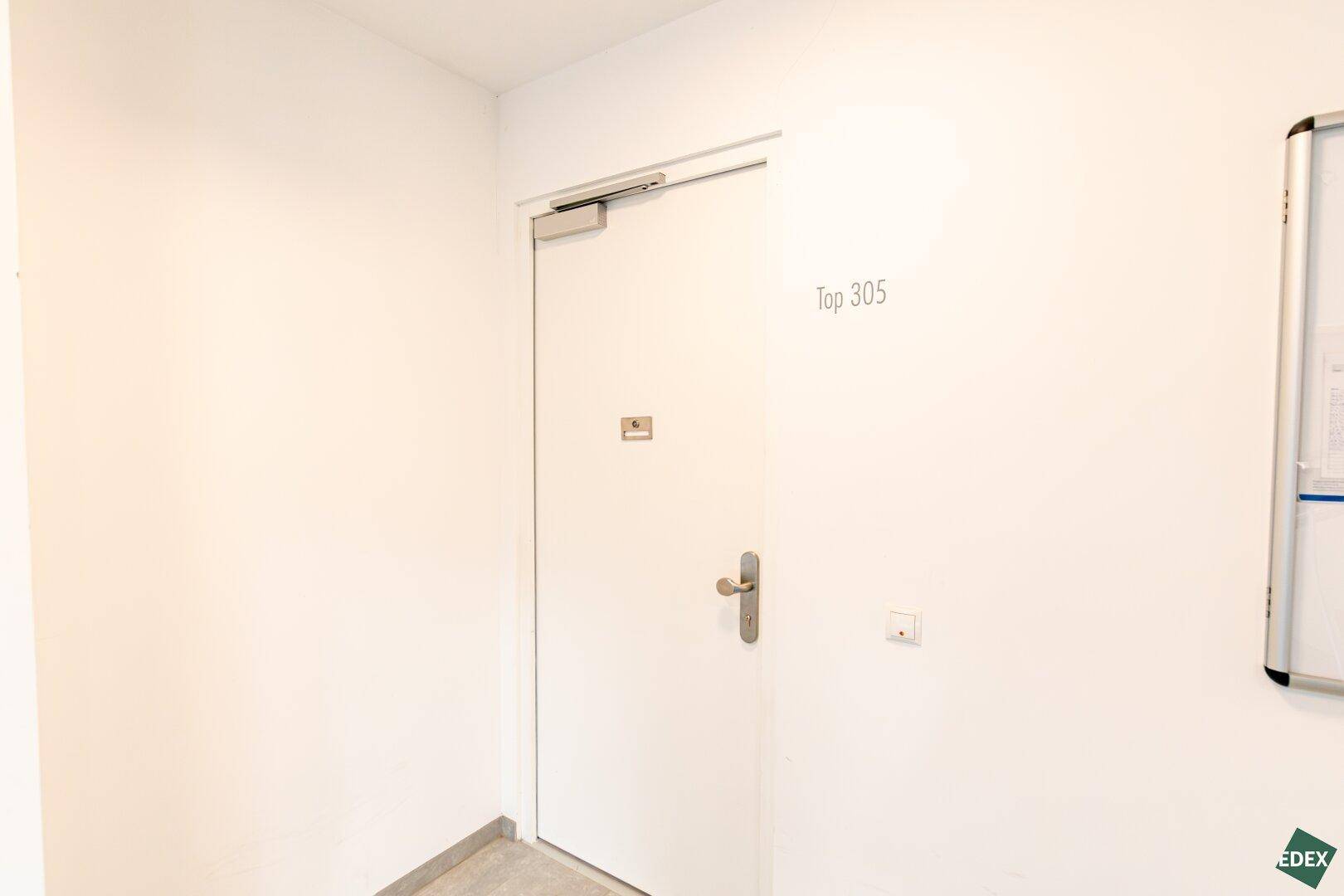 Eingangsbereich einer Wohnung mit weißer Tür und der Nummer "Top 305" an der Wand.