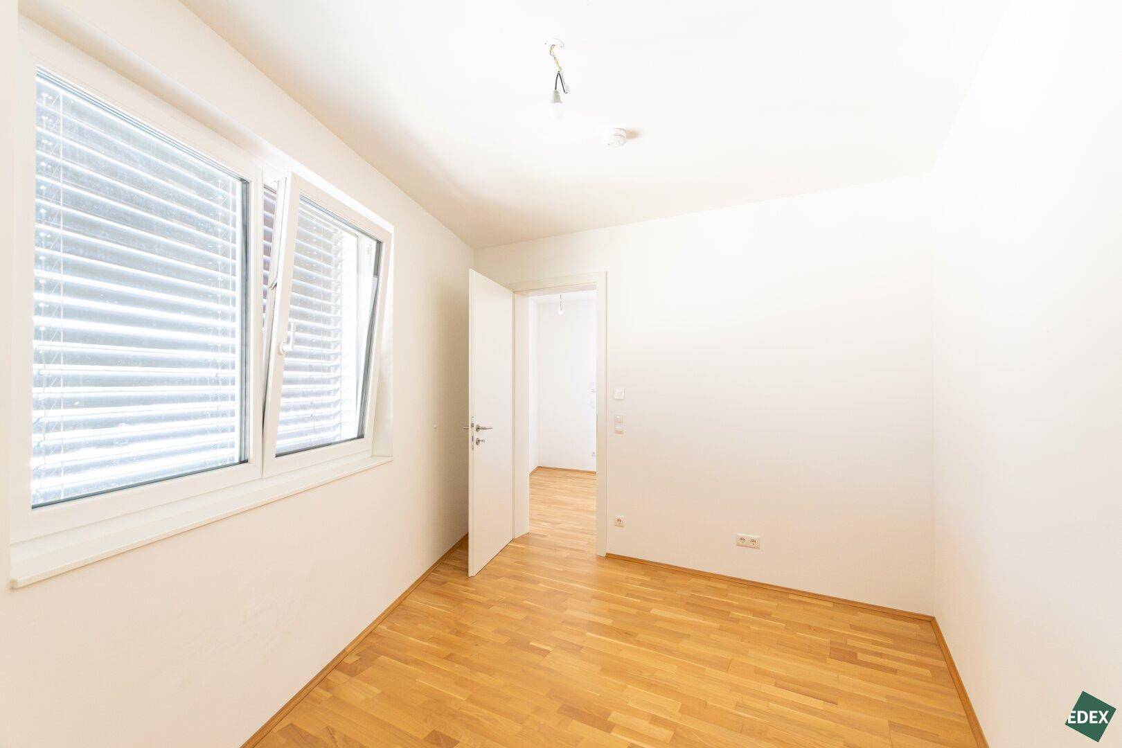 Helles Zimmer mit Parkettboden und einem großen Fenster, das sich zum Lüften öffnen lässt.