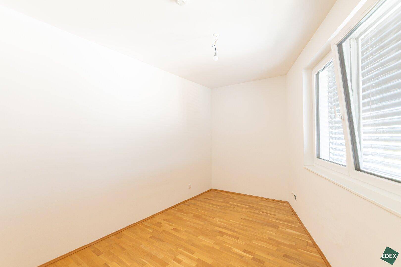 Schlichtes Zimmer mit Parkettboden und weiß gestrichenen Wänden, ideal als Kinder- oder Gästezimmer.