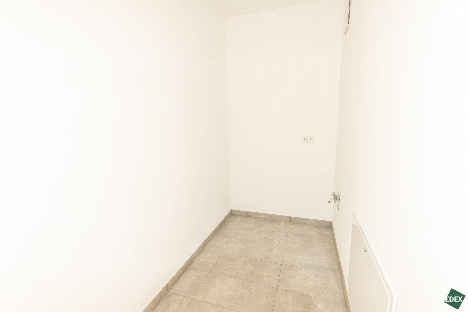 Praktischer Abstellraum mit Fliesenboden und Anschlüssen, ideal für Waschmaschine oder Lagerung.