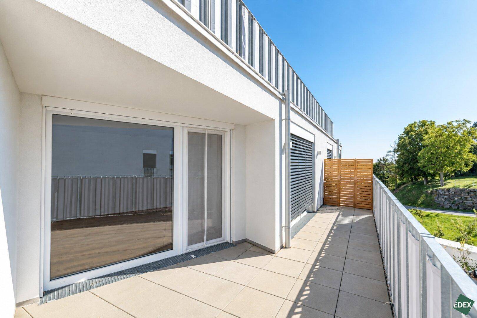 Lange, sonnige Terrasse mit Fliesenboden und Blick ins Grüne, ideal für Entspannung im Freien.