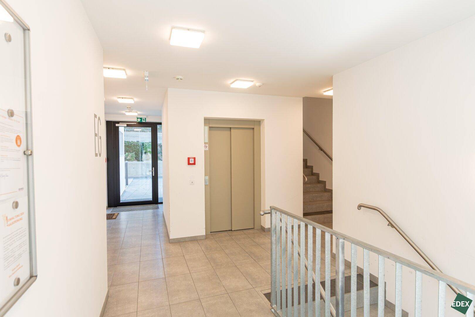 Heller Treppenhausbereich mit Aufzug und Treppe, führt zu den verschiedenen Etagen des Gebäudes.