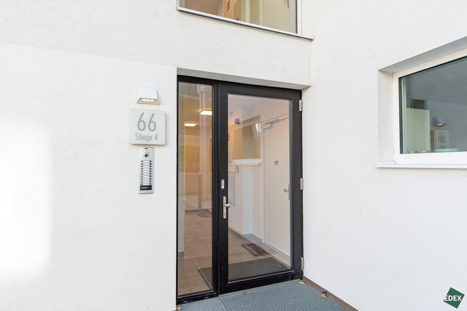 Moderner Hauseingang mit Glasfront und Gegensprechanlage, gut beleuchtet und zugänglich.