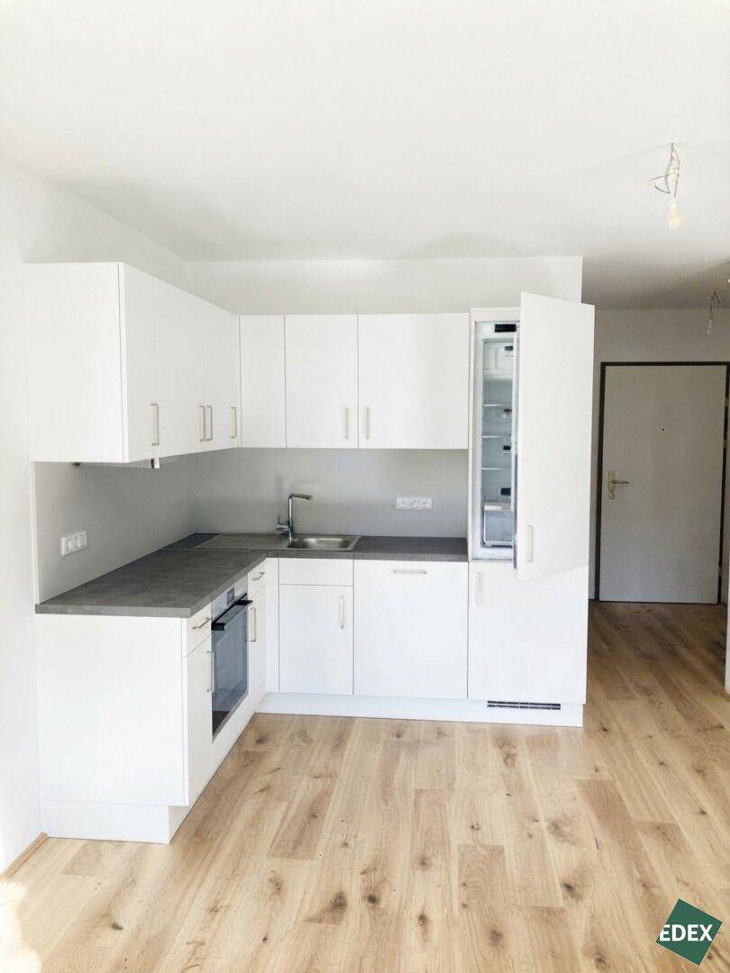 Moderne Einbauküche in Weiß mit grauer Arbeitsplatte und integriertem Kühlschrank.