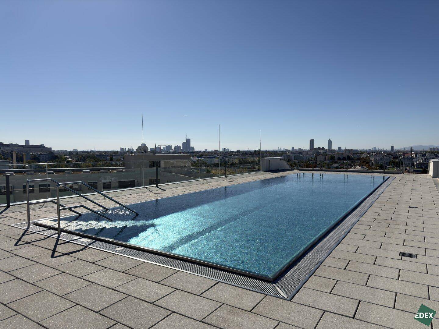 Atemberaubender Dachpool mit weitem Blick auf die Skyline der Stadt unter blauem Himmel.
