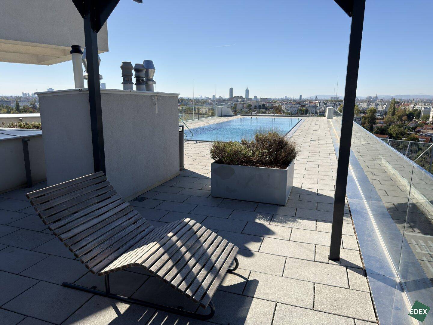 Entspannende Dachterrasse mit Liegestühlen, Blick auf den Pool und die Stadtlandschaft.
