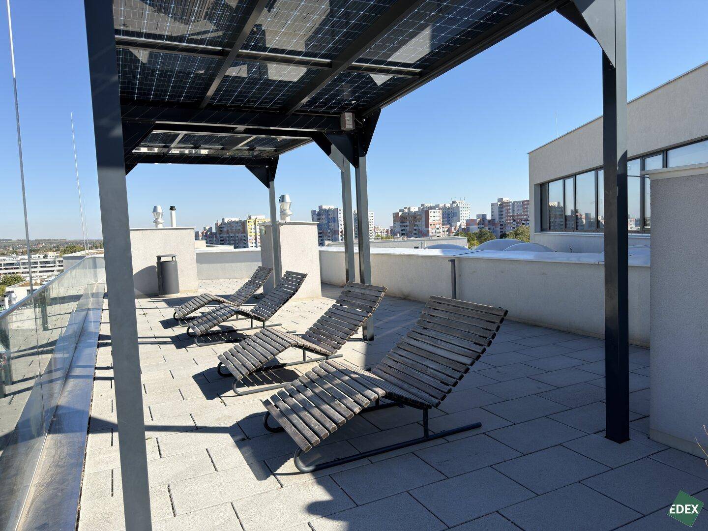 Sonnige Dachterrasse mit Liegestühlen unter einer Pergola mit integrierten Photovoltaik-Modulen.