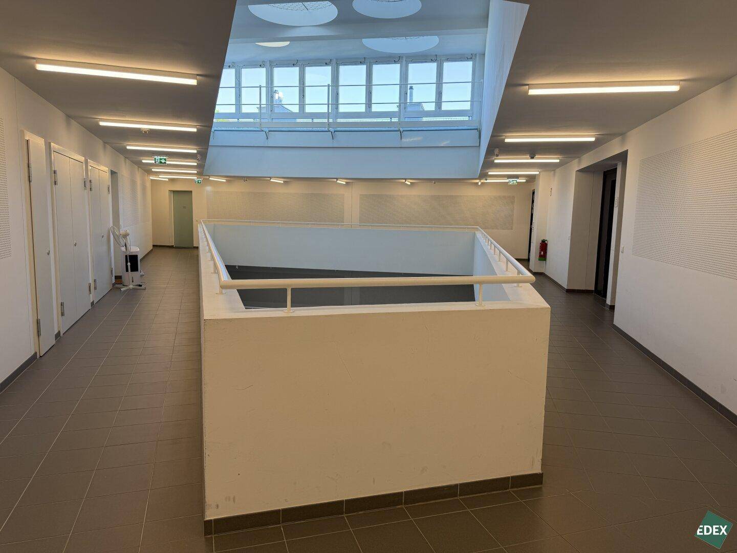 Geräumiger Flur mit Fliesenboden und einem offenen Atrium, das Tageslicht von oben hereinlässt.