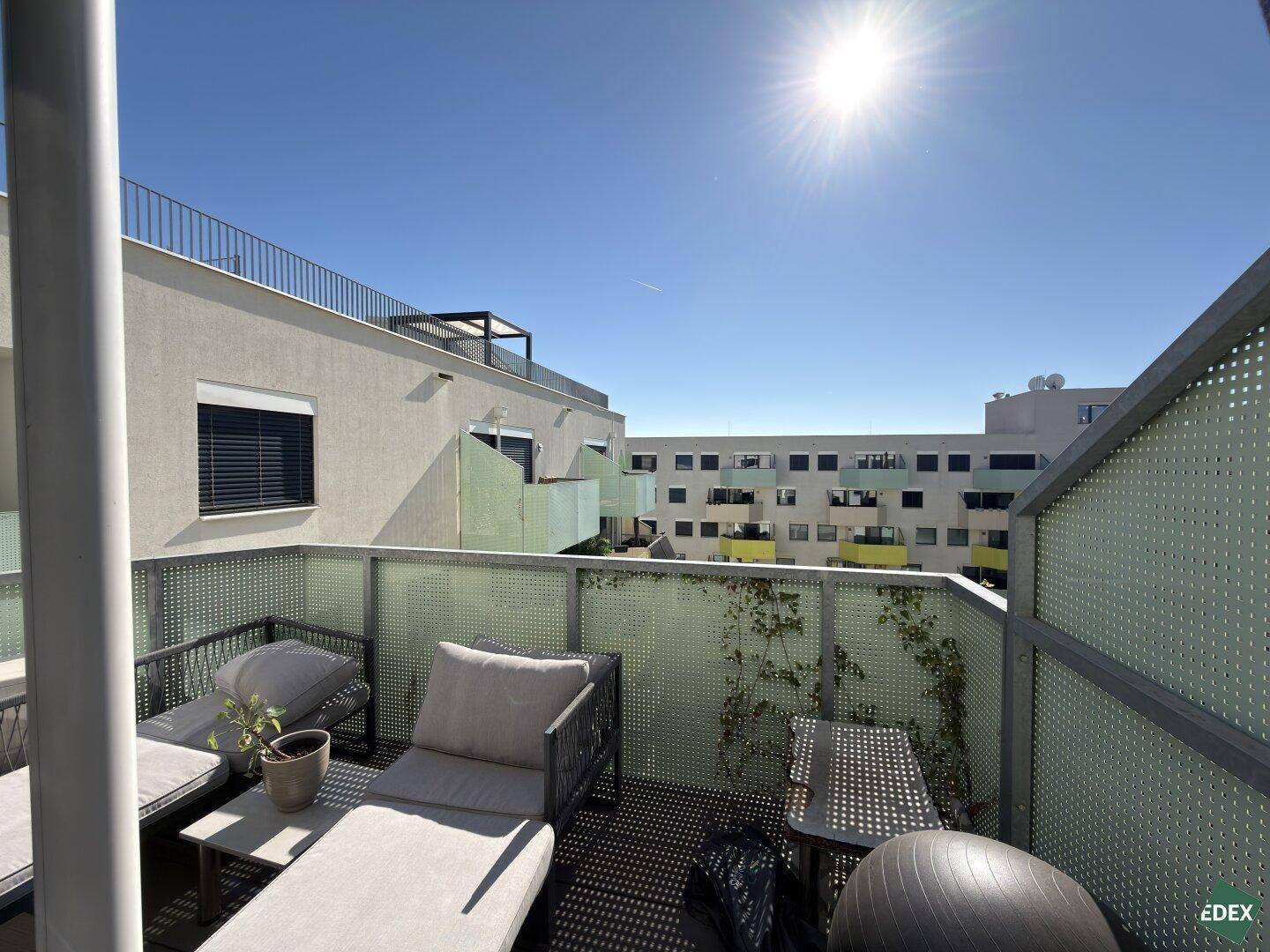 Sonniger Balkon mit bequemen Loungemöbeln und Blick auf die umliegenden Wohngebäude.