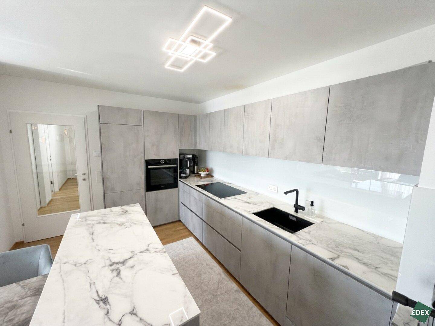 Detailansicht der modernen Küche mit integriertem Backofen, Induktionskochfeld und eleganten Marmor-Arbeitsplatten.
