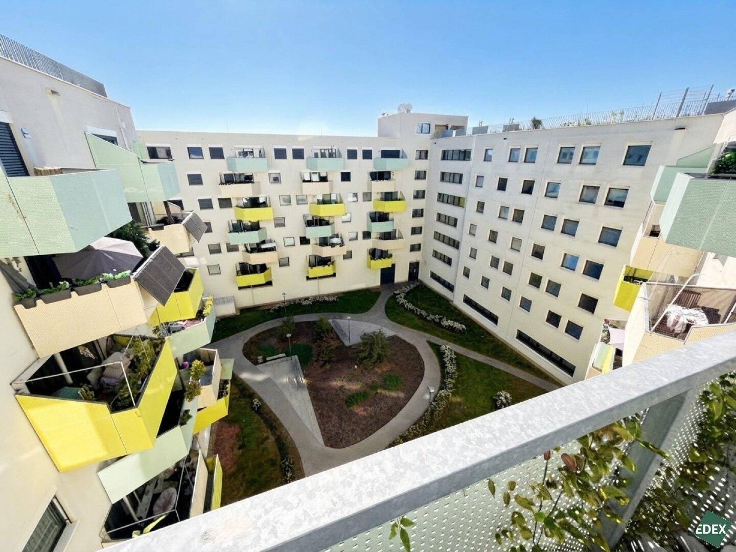 Blick auf den begrünten Innenhof der Wohnanlage, umgeben von modernen Gebäuden mit Balkonen.