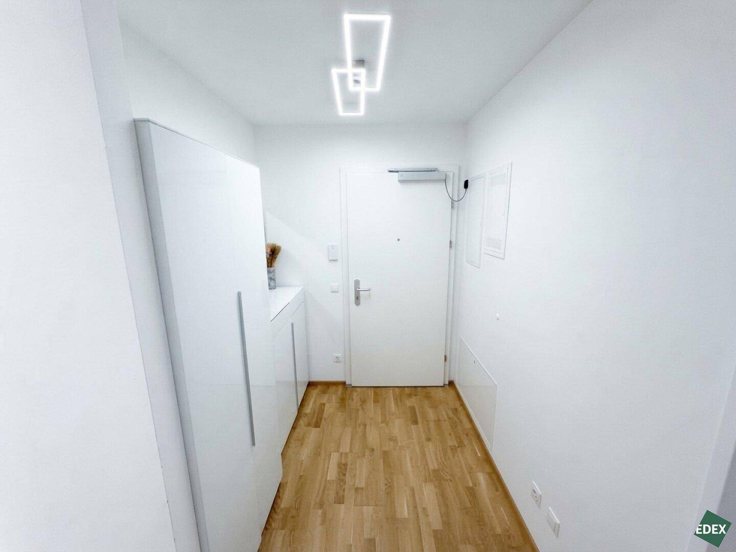 Heller Eingangsbereich mit Holzboden und modernen Deckenleuchten, einladend und funktional gestaltet.